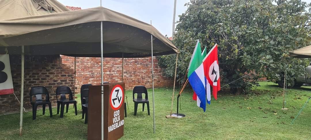 AWB Podium en stoele onder ’n tent met organisasievlae op ’n grasperk.